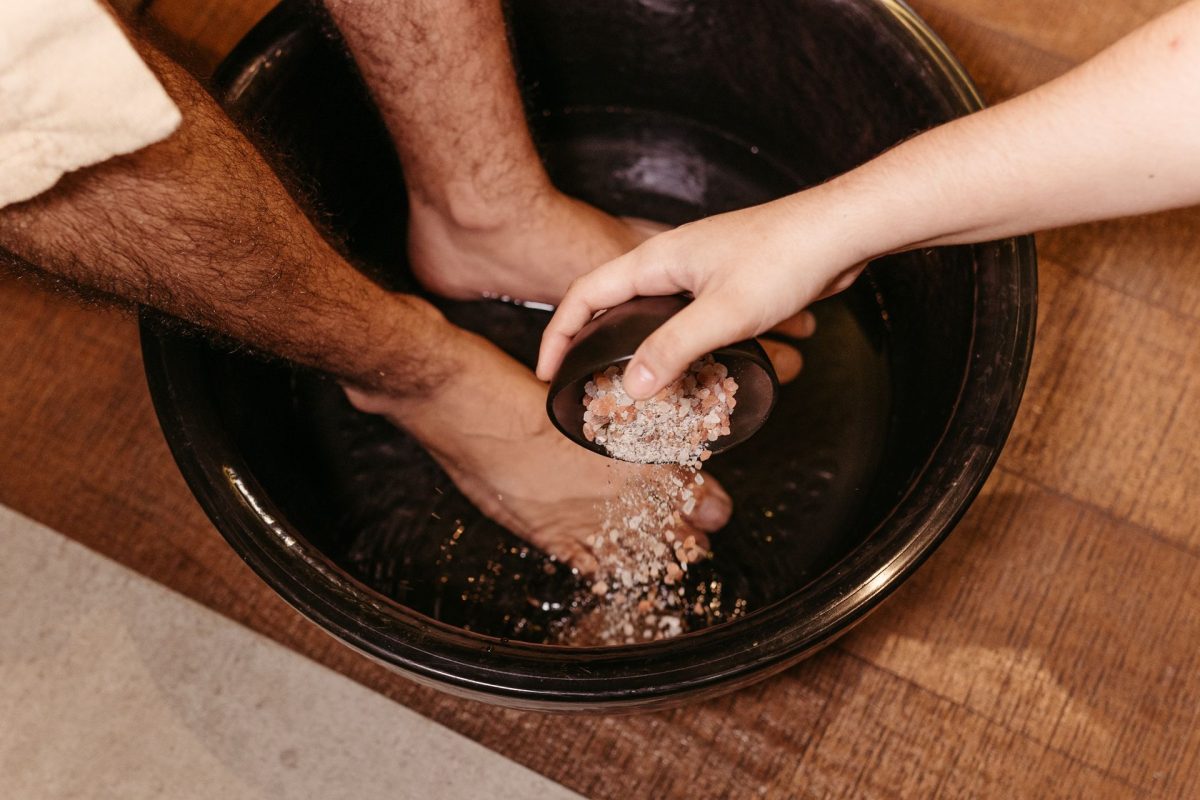 Feet in a warm foot bath as the therapist adds sea salt before a Thai foot massage